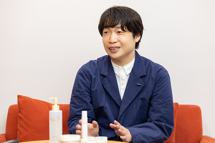 Ozawa speaking in front of Perfect Cover products while seated on a red sofa.