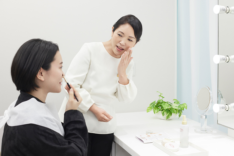 Aoki conducts a makeup lesson using Perfect Cover for a customer seated in front of a mirror at the Shiseido Life Quality Beauty Center.