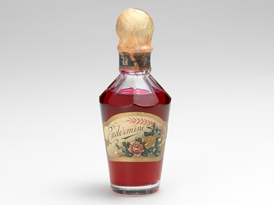 1897年に資生堂初の化粧水として誕生した「オイデルミン」の画像。赤色の化粧水が入った瓶に、資生堂を象徴する椿のイラストが描かれたラベルが貼られている。