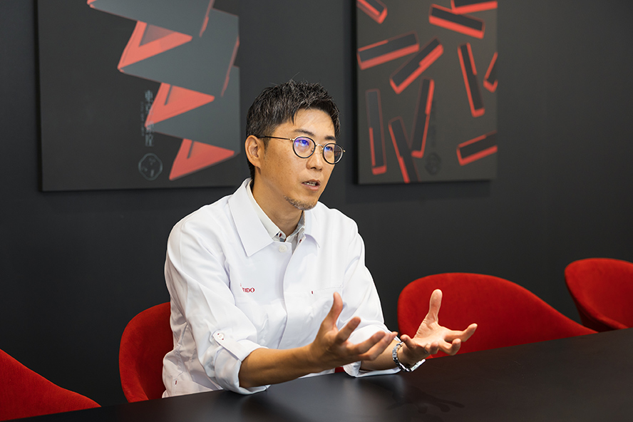 資生堂研究員である小橋が椅子に座り、真剣な表情で語っている
